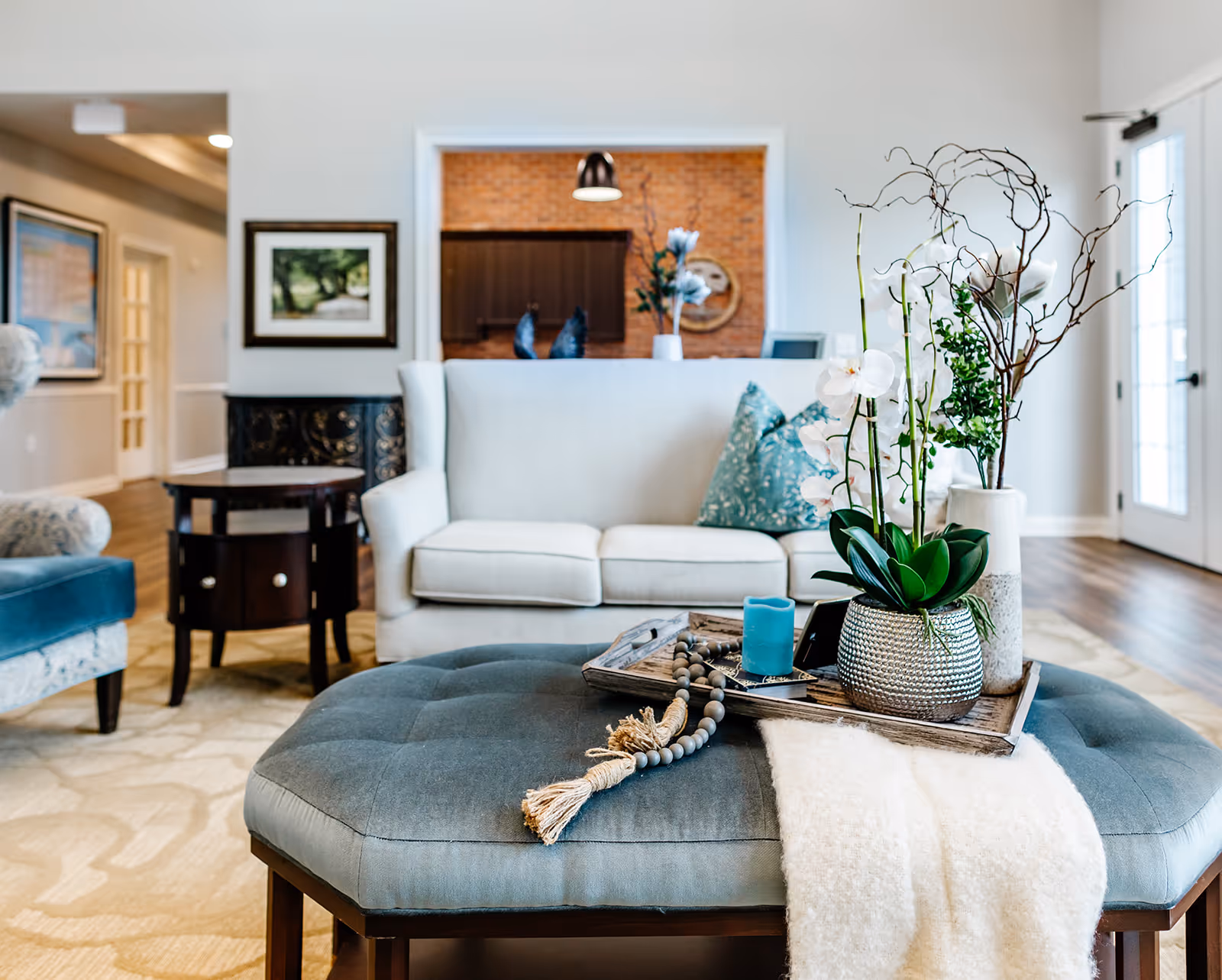 Bright, modern living room with a sofa, ottoman topped by a decorative tray with plants and accessories, and nearby accent chairs.