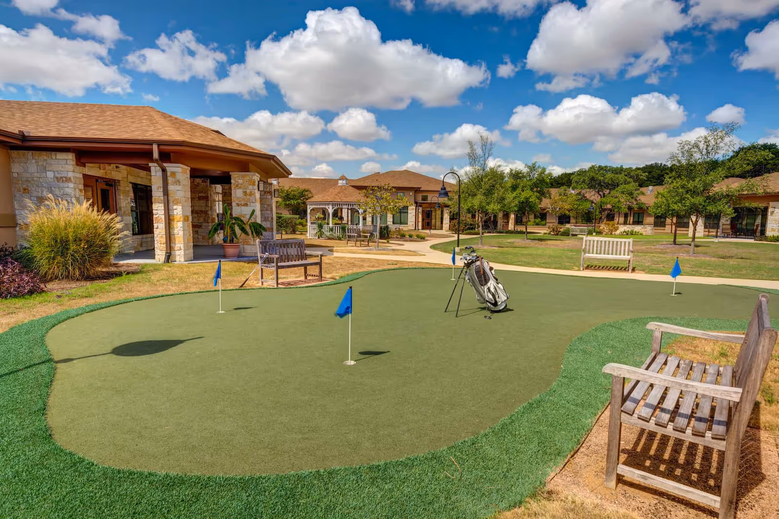 Outdoor putting green with flags, benches and a golf bag in the courtyard of a senior living community.