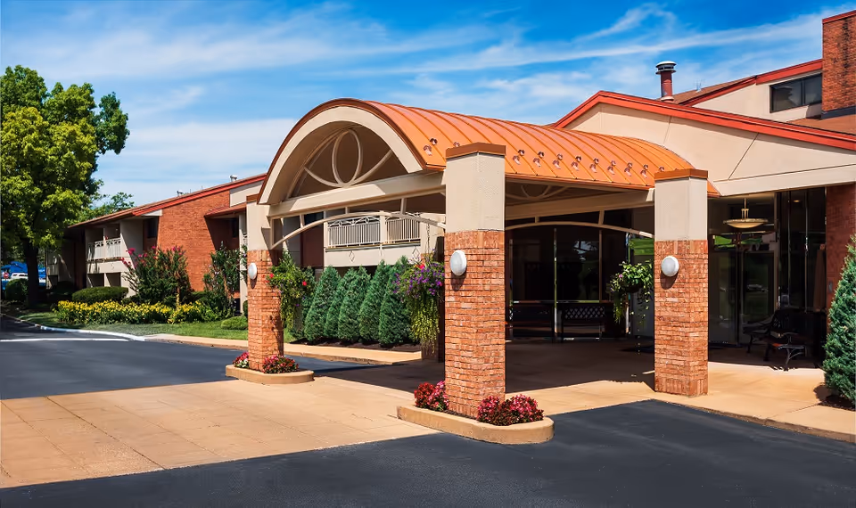 Senior living facility entrance with brick columns, curved arch, and glass doors.