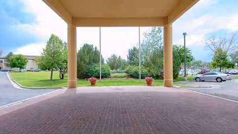 Covered driveway with brick paving and beige columns at the Cherry Creek Retirement Village entrance.