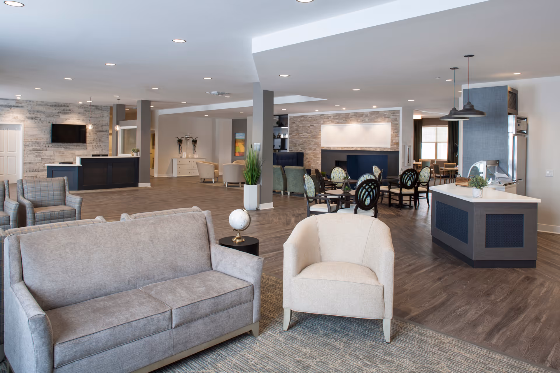 Spacious modern common lounge with sofas, armchairs, dining tables and a serving counter in a senior living facility.