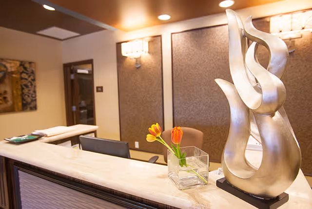 Reception desk area with a decorative silver sculpture, a small vase of tulips, a computer monitor, and warm wall sconces.