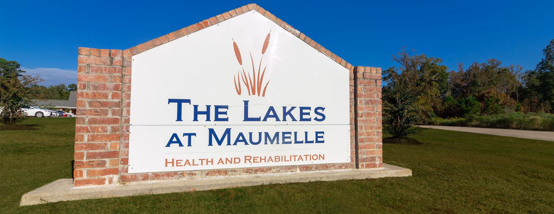 An exterior brick-framed sign for 'The Lakes at Maumelle Health and Rehabilitation' on a grassy area.