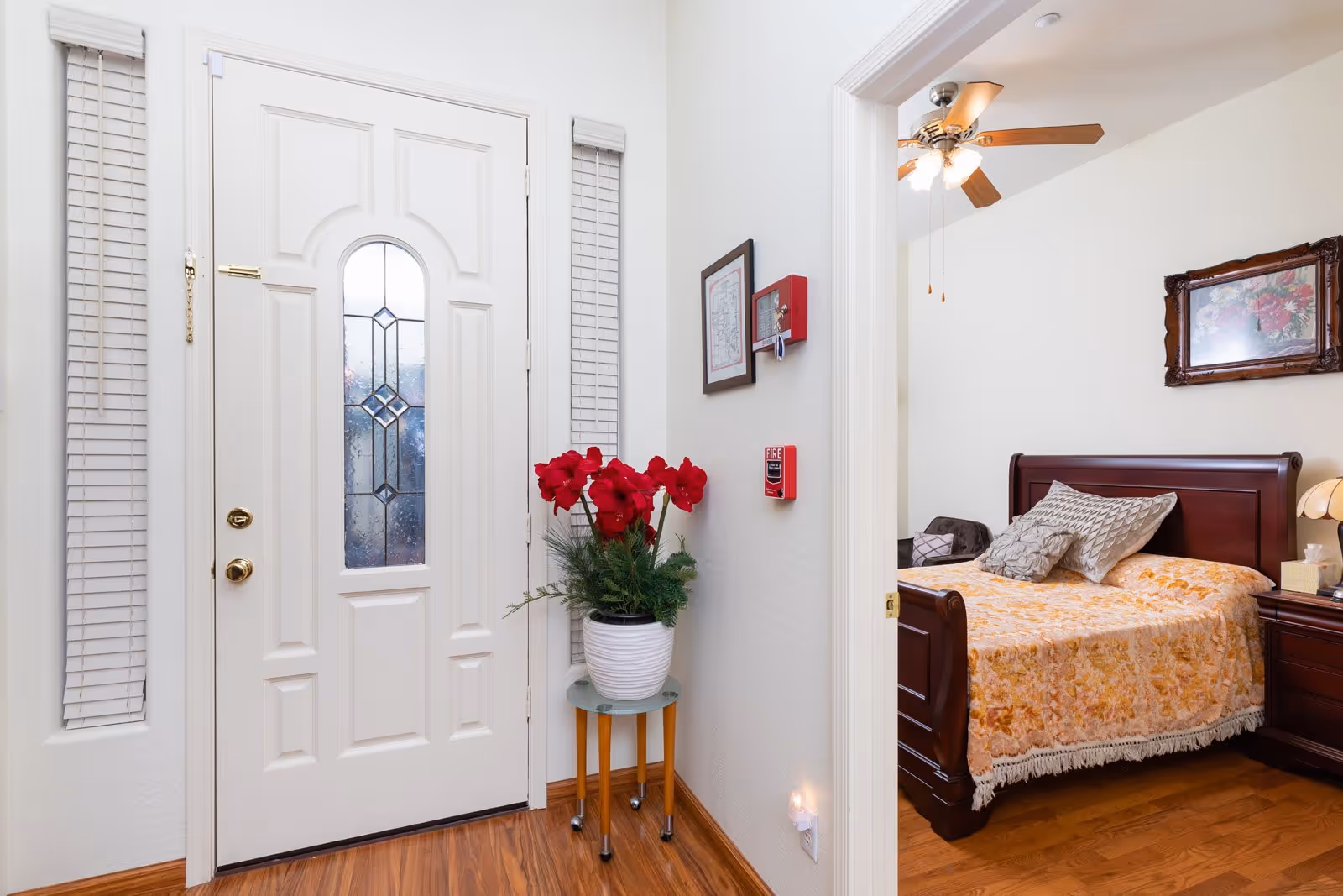 Interior entryway with a white front door, a potted plant on a small table, and a view into a furnished bedroom.