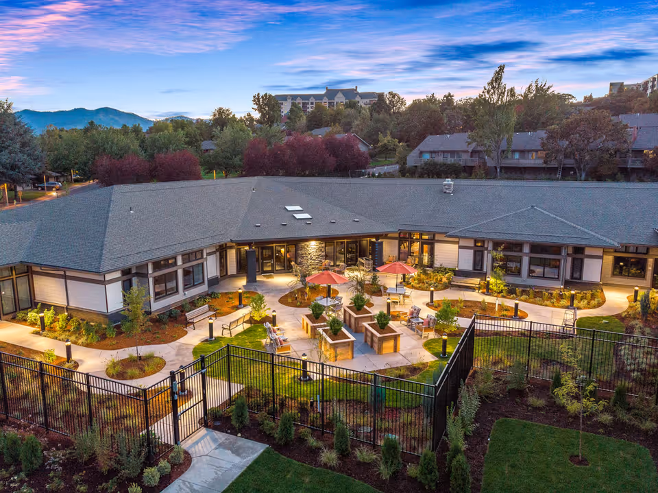 Aerial view of a U-shaped senior living building with a landscaped central courtyard, seating areas, umbrellas and outdoor lighting at dusk.