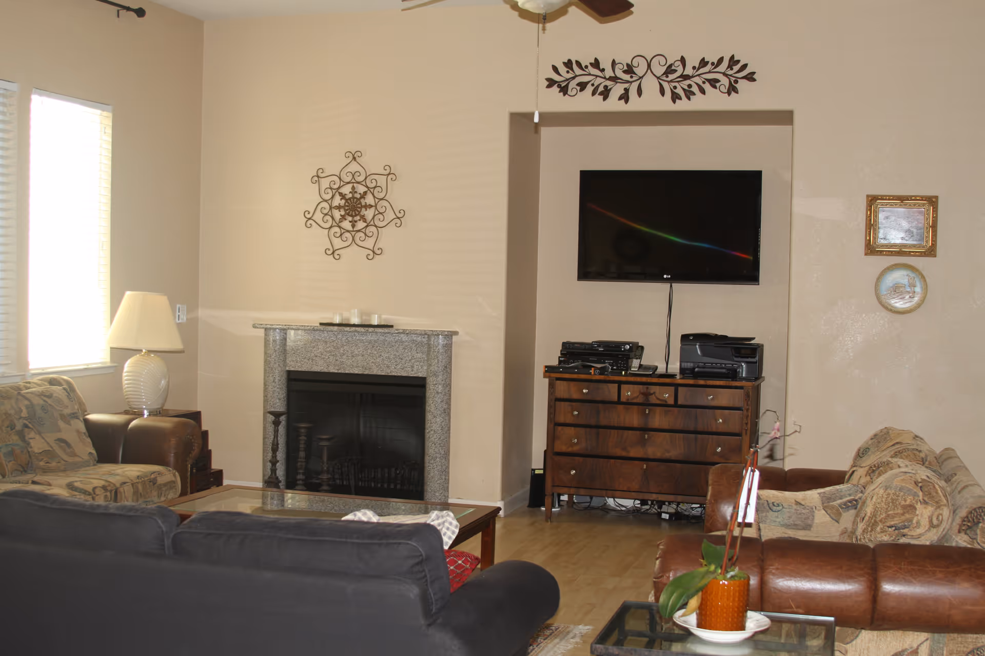 Living room with sofas and armchairs arranged around a fireplace, a wall-mounted TV above a wooden dresser, and a coffee table in front.