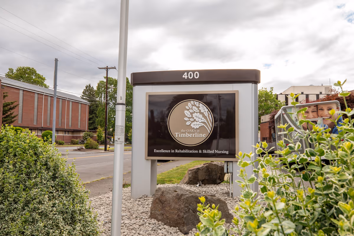 Outdoor entrance sign for The Oaks at Timberline (400) with landscaping and the facility in the background.