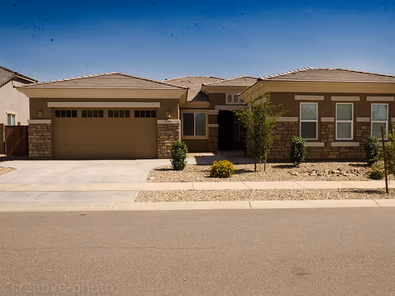 Front exterior of a single-story suburban house with a two-car garage, driveway, and desert landscaping.