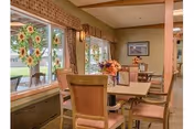 Small dining room with a table and chairs, floral centerpieces, and large windows decorated with sunflower decals.