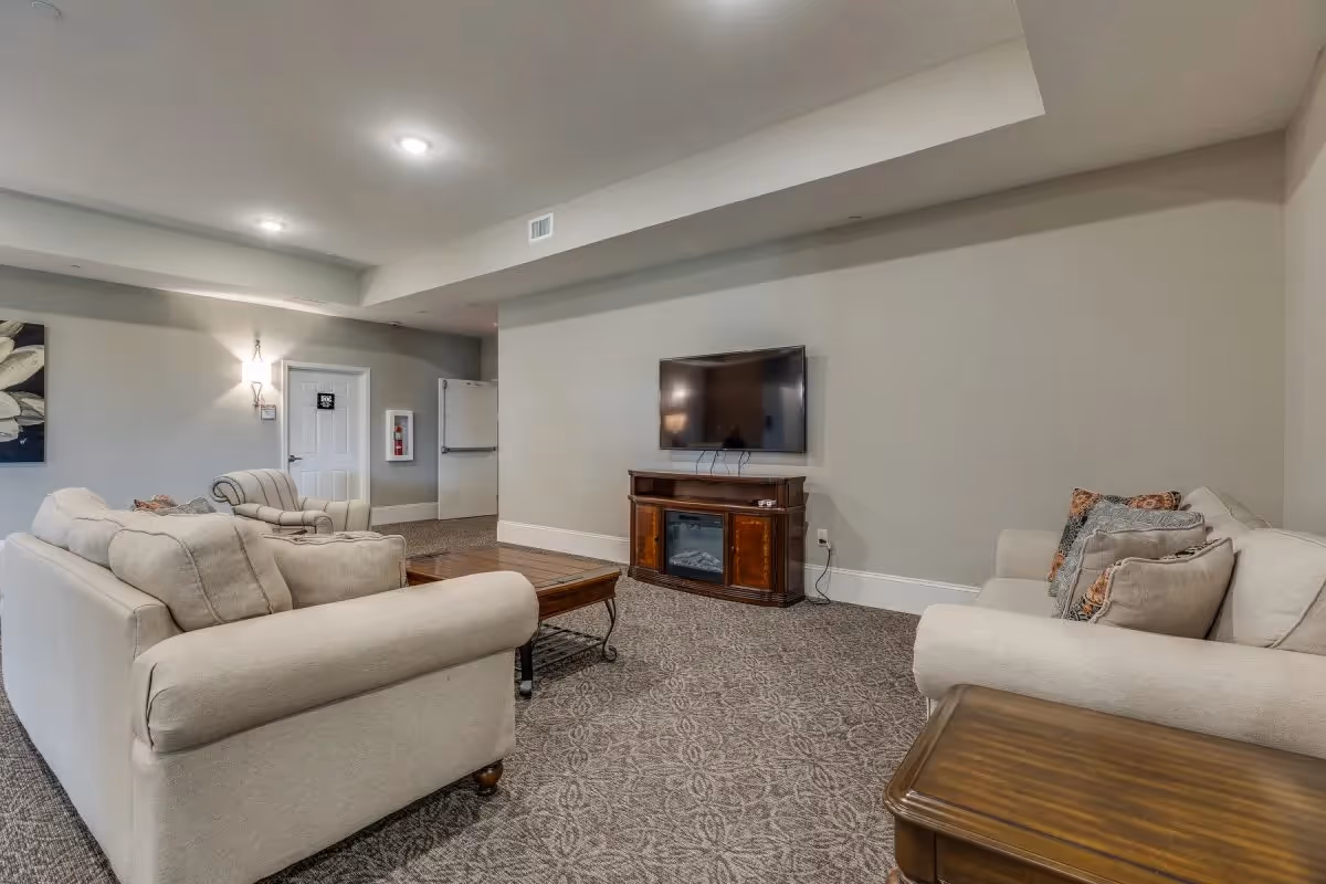 Cozy lounge with beige sofas and armchairs facing a wall-mounted TV above a wooden console in a neutral-toned room.
