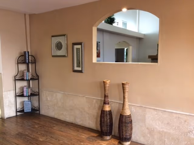 Interior hallway with beige walls, arched window opening, bookshelf, and tall woven vases.