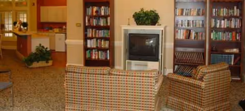 Cozy communal living room with striped armchairs, a TV, and bookshelves.
