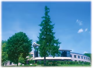 Modern senior living facility building with curved facade, trees, and a blue sky.