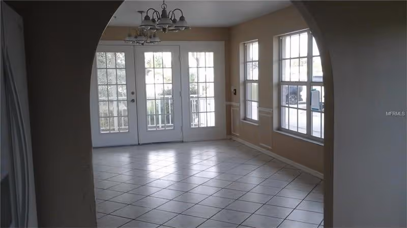 Empty tiled dining area seen through an arched doorway with hanging light fixtures, French doors and multiple windows.