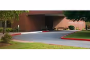 Front entrance of a brick building with a curved driveway, benches, and landscaped lawn.