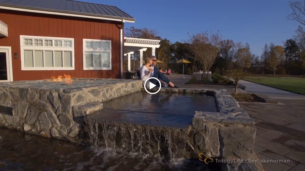 Outdoor plaza featuring a stone water feature with a small waterfall in front of a red building and two people sitting at the water's edge.