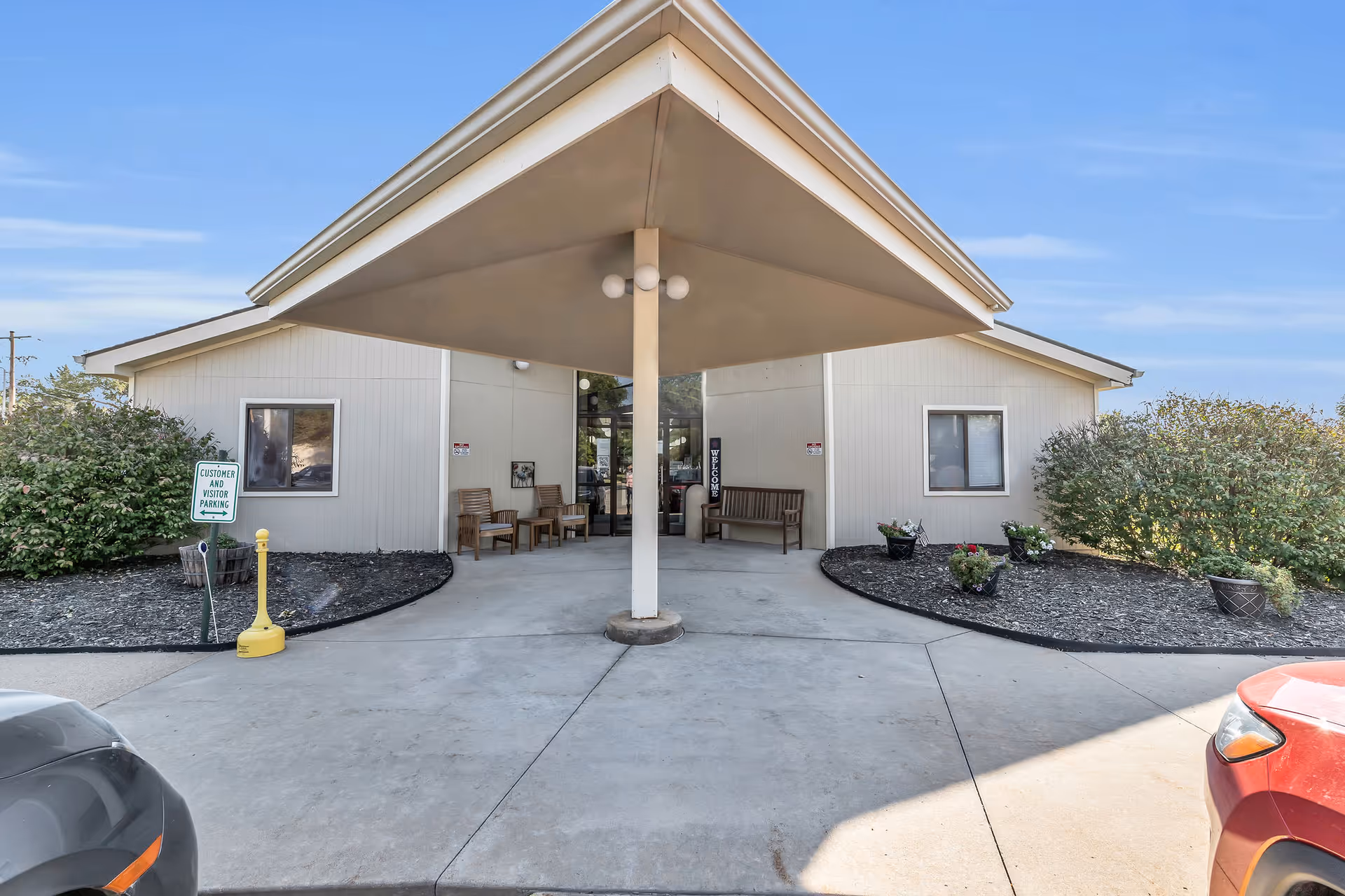 Front entrance of a single-story healthcare facility with a covered drop-off canopy, benches, and landscaped planters.