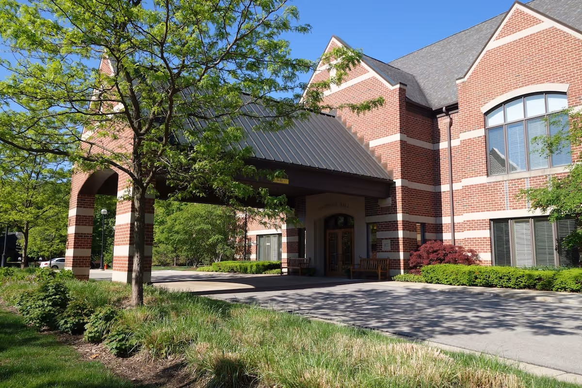 Covered entrance/porte-cochère of a red-brick building with trees and landscaped grounds.