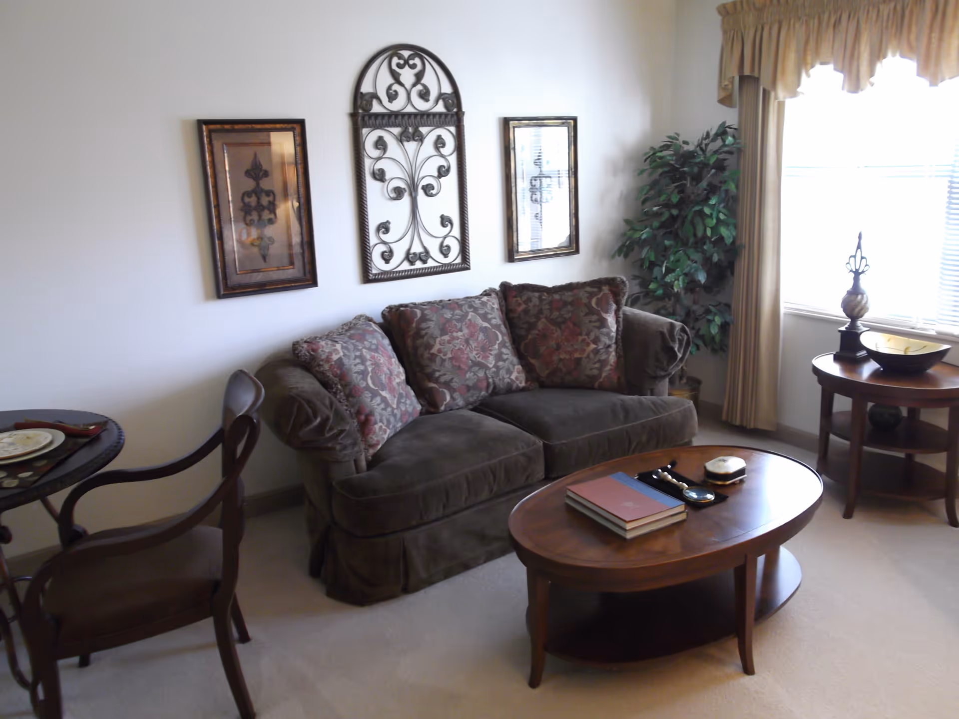 Cozy living room with a sofa, patterned cushions, a wooden coffee table, side tables, wall art and a window with curtains.