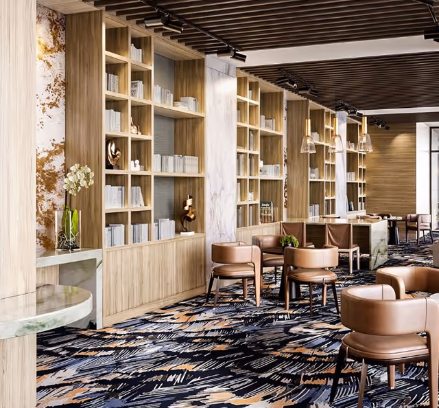 A modern lounge area with wooden bookshelves filled with books and decorative items, brown leather chairs arranged around small tables, and a patterned carpet. The ceiling features wooden slats with track lighting and pendant lights hanging over a counter area.