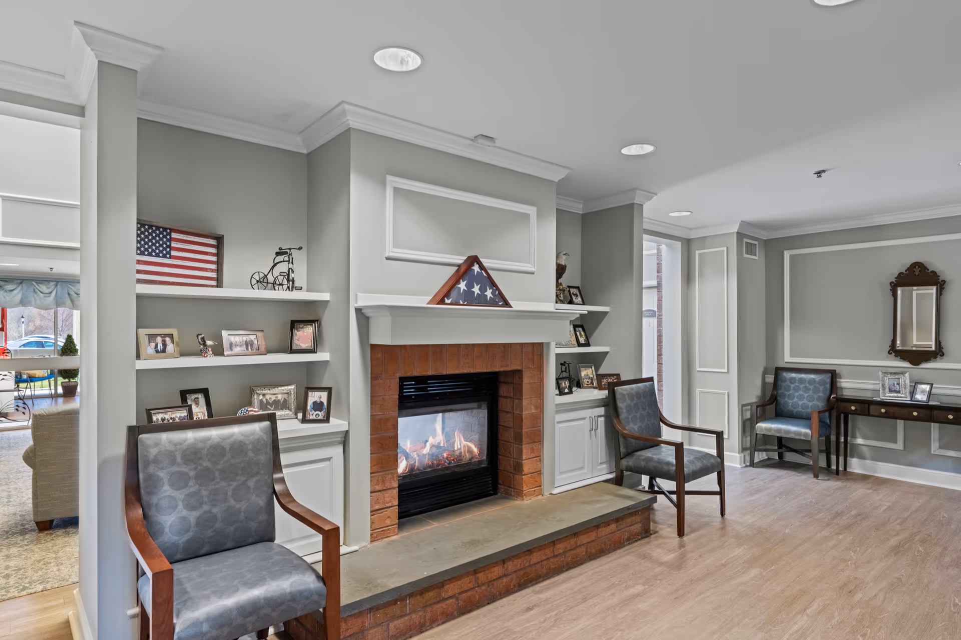 Comfortable senior living common room with a lit fireplace, shelving of framed photos, and several chairs.