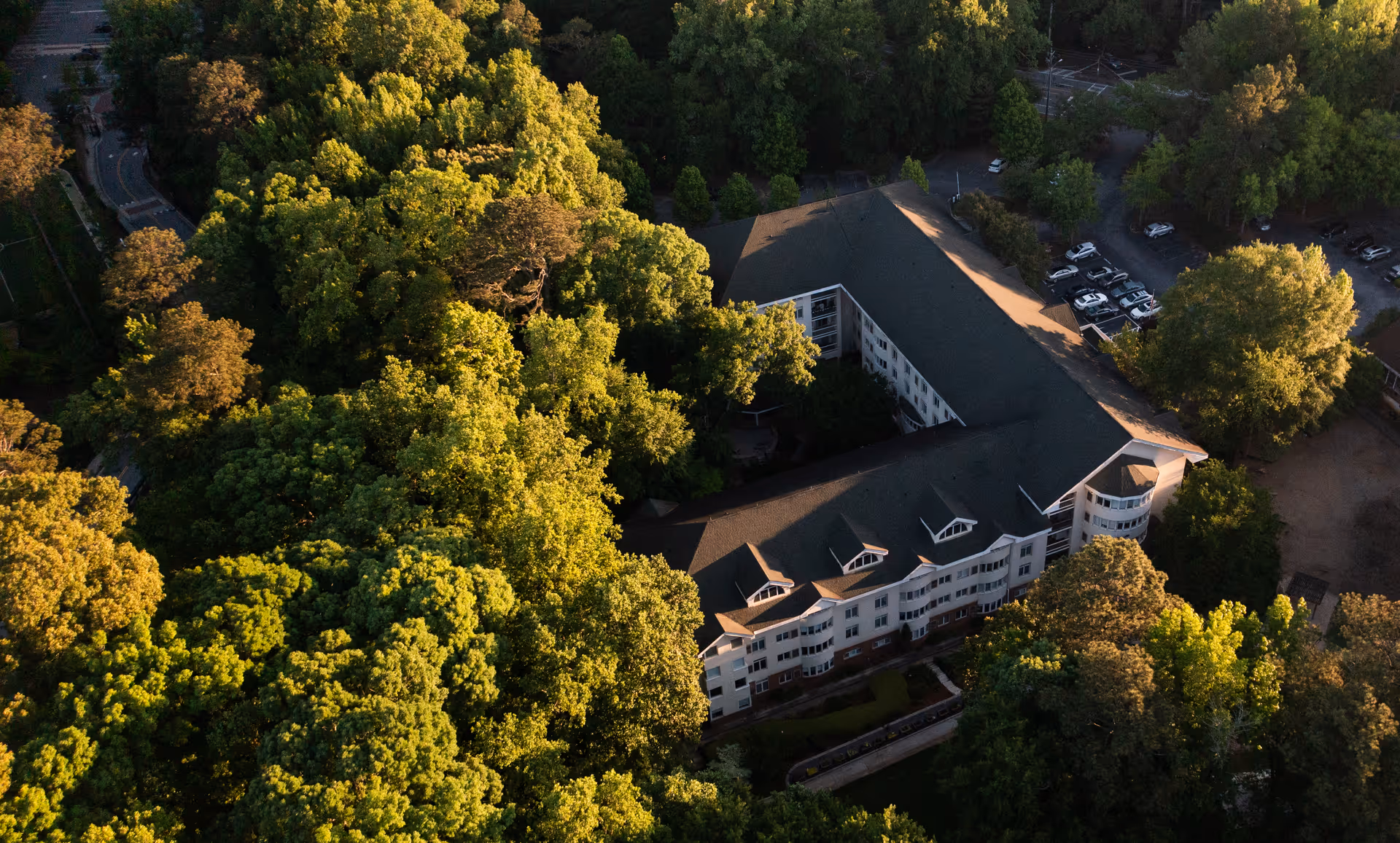 Aerial view of Saint Anne's Terrace, a large multi-story building surrounded by dense green trees and a parking area with several cars visible.