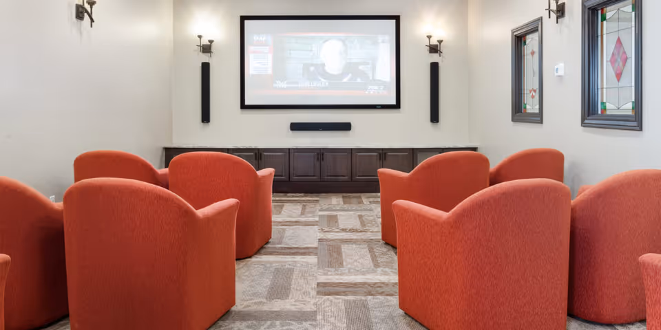 Small screening room with rows of red upholstered armchairs facing a wall-mounted projector screen.
