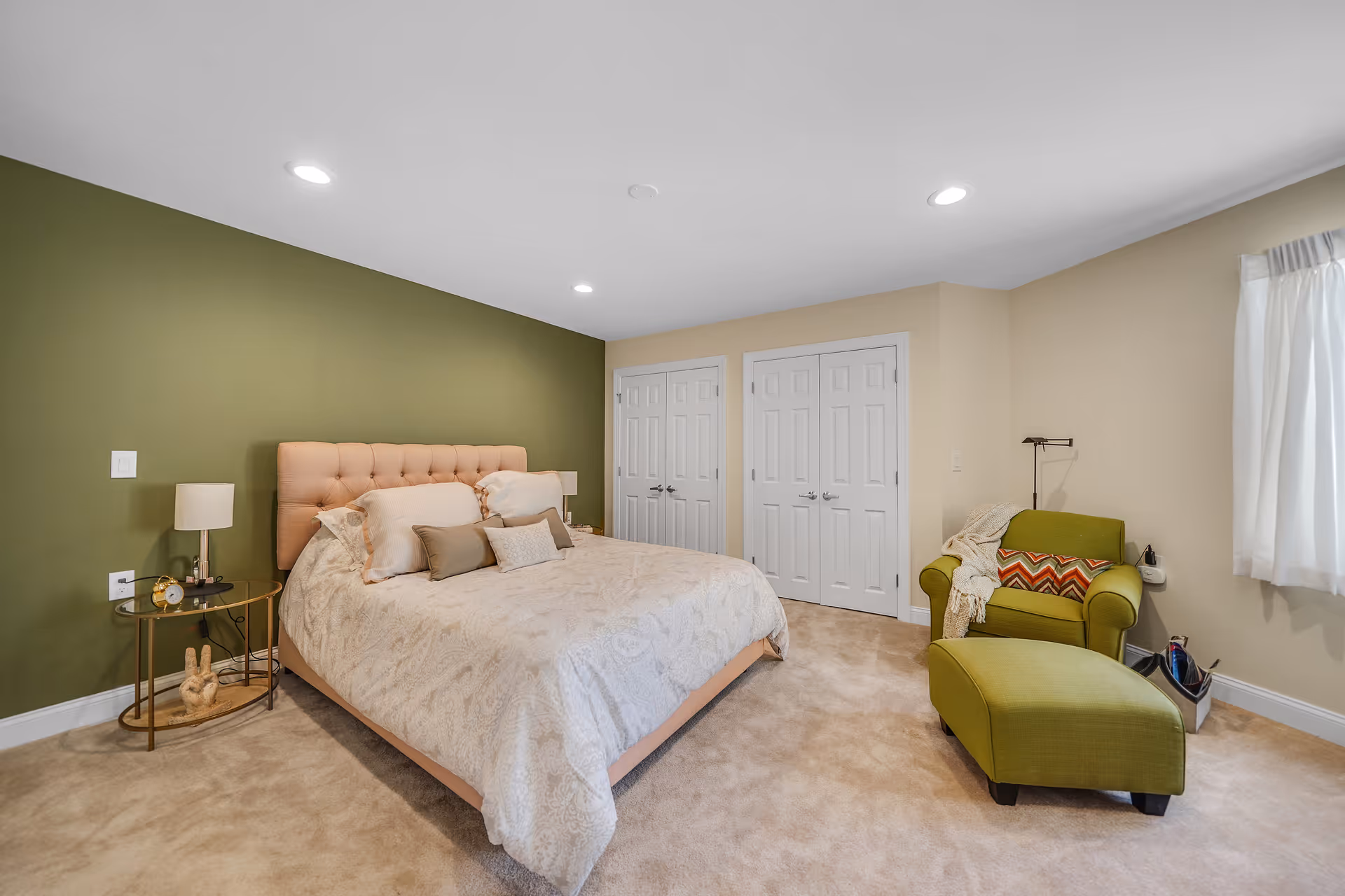 Spacious bedroom with a tufted bed against a green accent wall, bedside tables, and a green armchair with ottoman.
