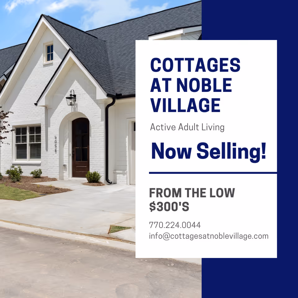 Exterior view of a white brick cottage with a dark shingled roof, a wooden front door with an arched entryway, and a small landscaped area with grass and shrubs.