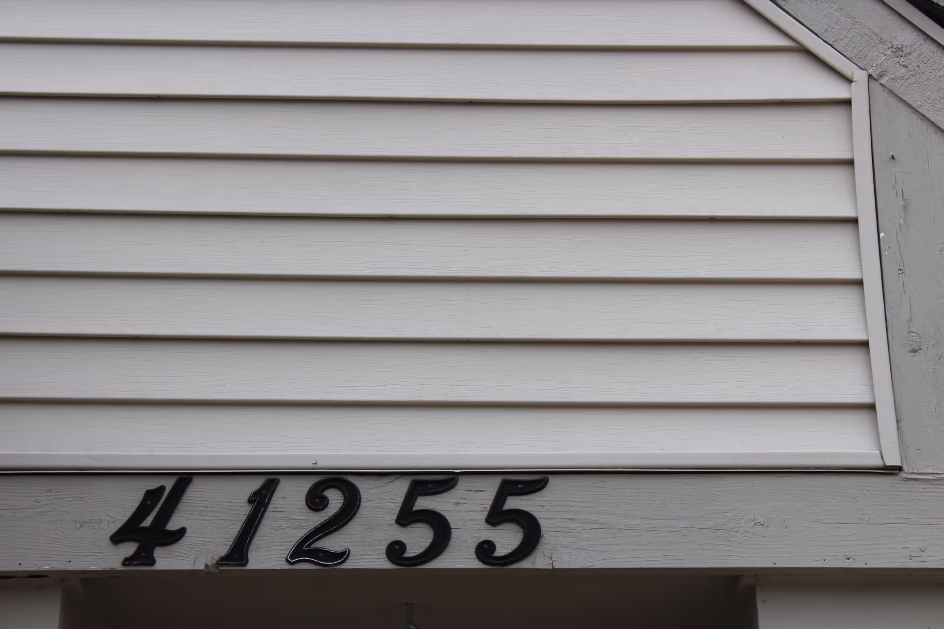 Close-up view of a building exterior wall with horizontal beige siding and the black house number 41255 mounted on a wooden beam below the siding.