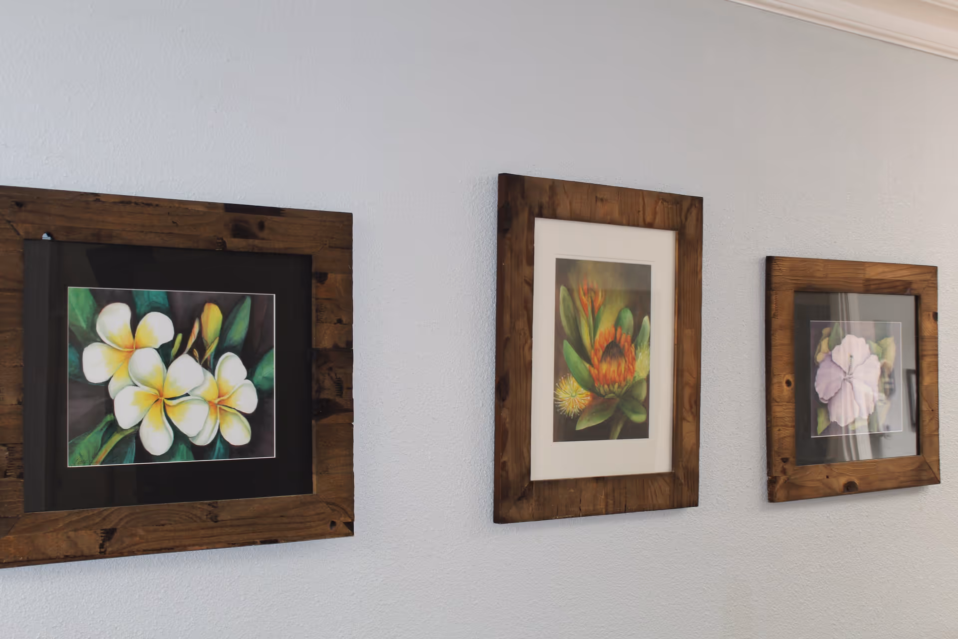 Three wooden-framed floral paintings hung on a pale wall.