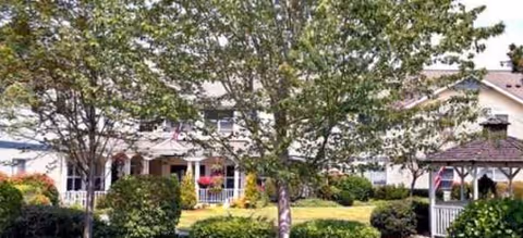 Brookdale Monroe exterior with landscaped lawn, trees, and a gazebo by the front porch.