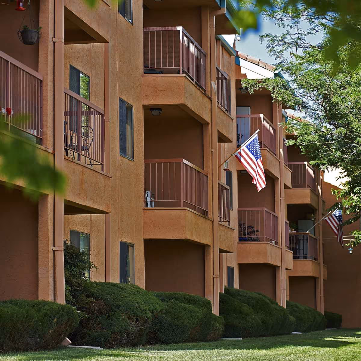 Exterior view of a multi-story senior living building with balconies, American flags, and landscaped shrubs.
