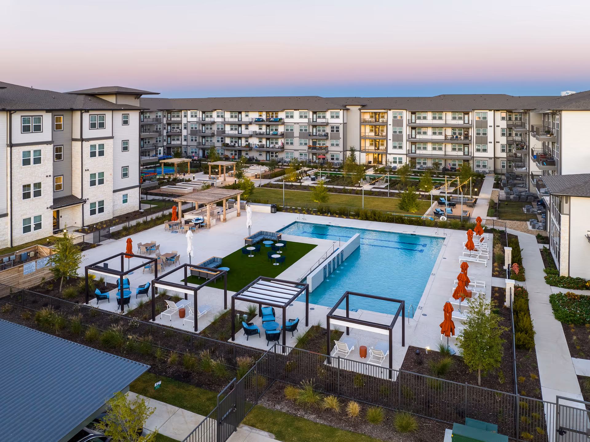Aerial view of a senior living community courtyard with a central swimming pool, cabanas, seating areas, and surrounding apartment buildings at dusk.