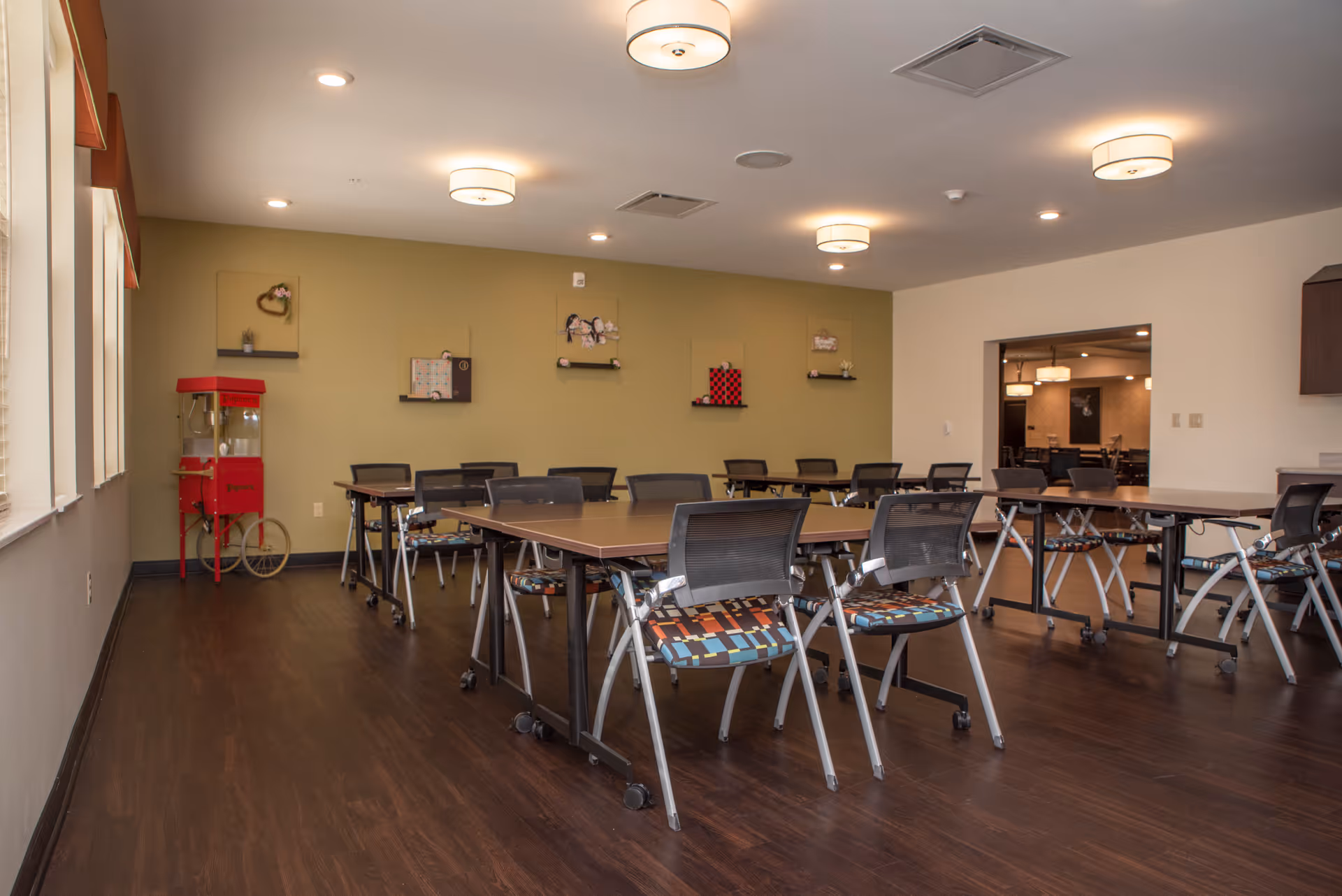Spacious multipurpose dining/activity room with rows of tables and chairs and a red popcorn machine against a green accent wall.