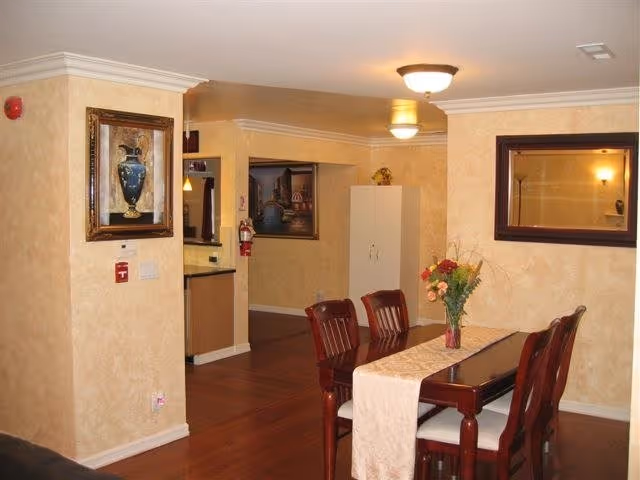 Warmly lit dining area with a wooden table and six chairs, a floral centerpiece, and framed artwork on textured beige walls.