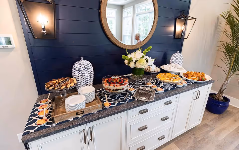 A buffet spread of desserts and hors d'oeuvres on a sideboard beneath a round mirror and wall sconces.