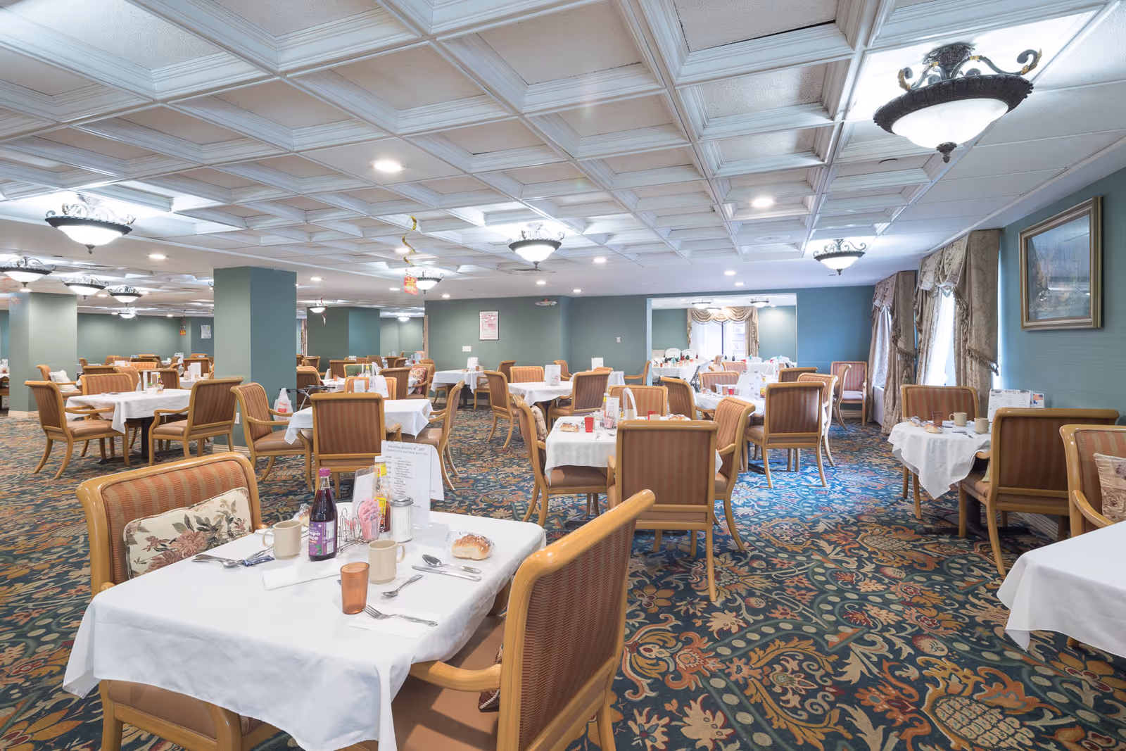 A spacious dining hall in a senior living facility with multiple tables set for meals.