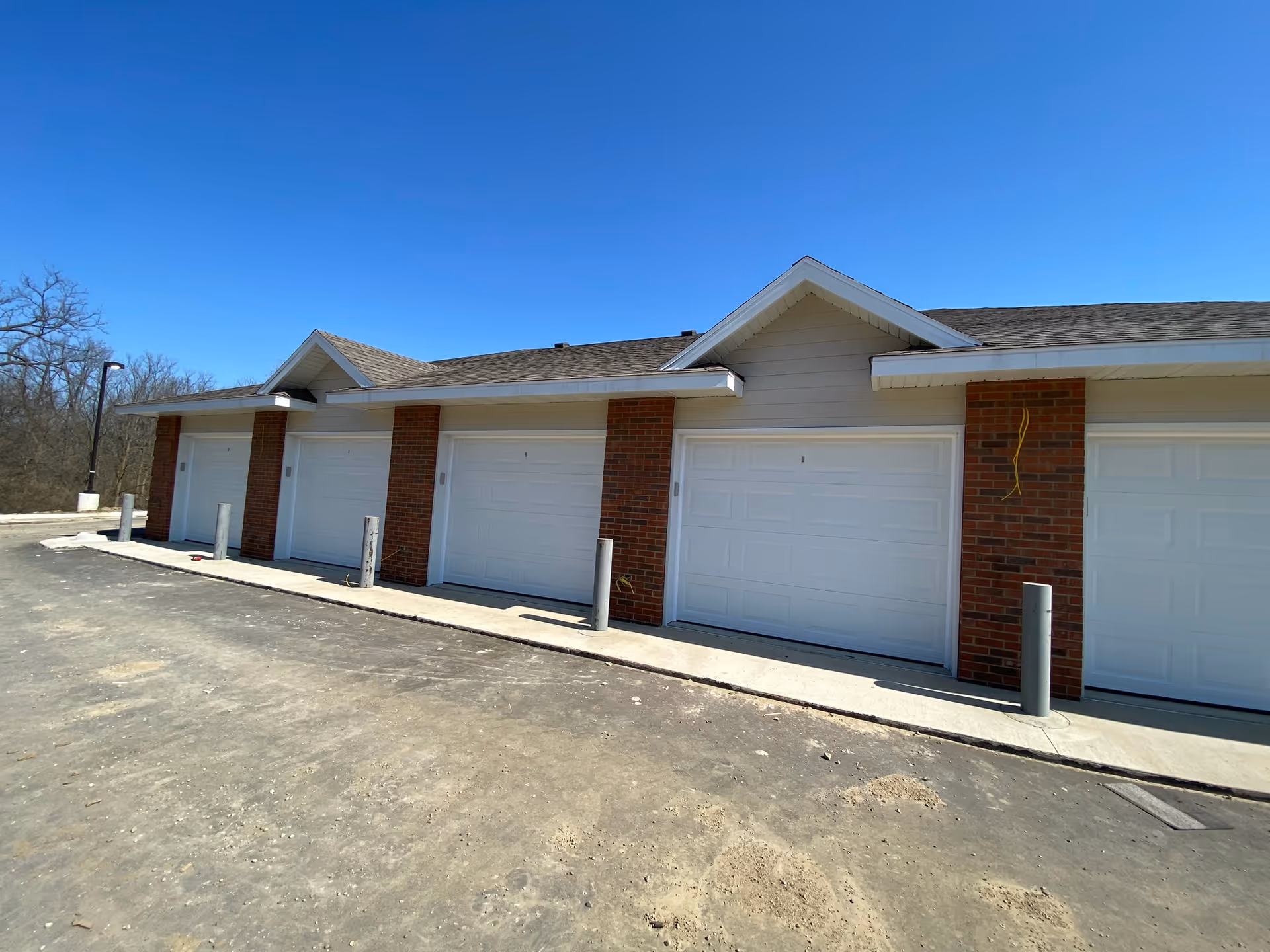 Row of attached white garage doors with brick columns and bollards in front under a clear blue sky.