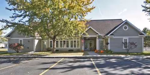 Front view of a single-story senior living facility with parking and trees.