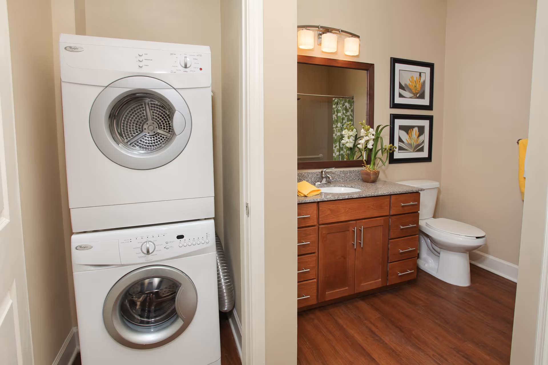 Stacked washer and dryer next to a bathroom with a wooden vanity, mirror, and toilet.