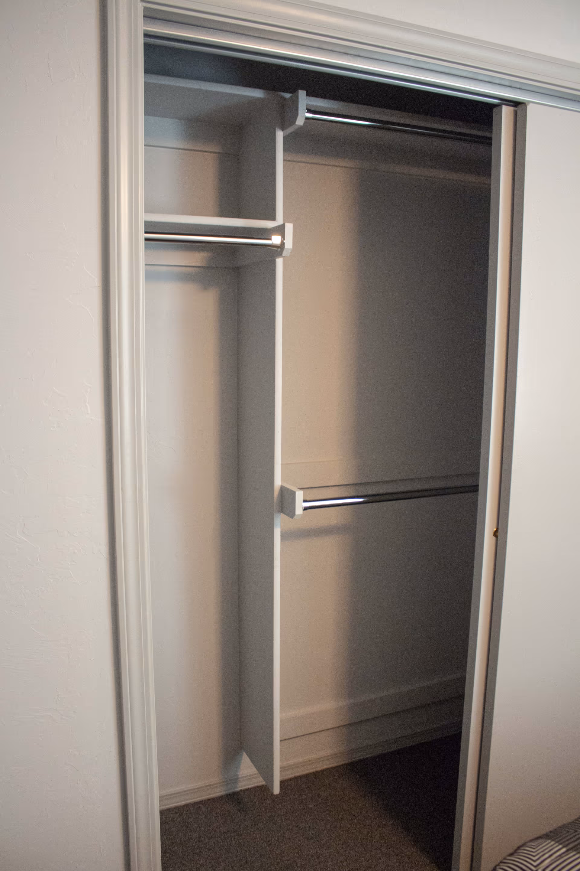 Empty closet with white sliding doors, featuring multiple metal hanging rods and a vertical divider inside.
