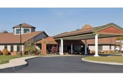 Front exterior view of Woodbrook Assisted Living Residence, Inc. building with a covered entrance, a circular driveway, and landscaped grounds under a clear sky.
