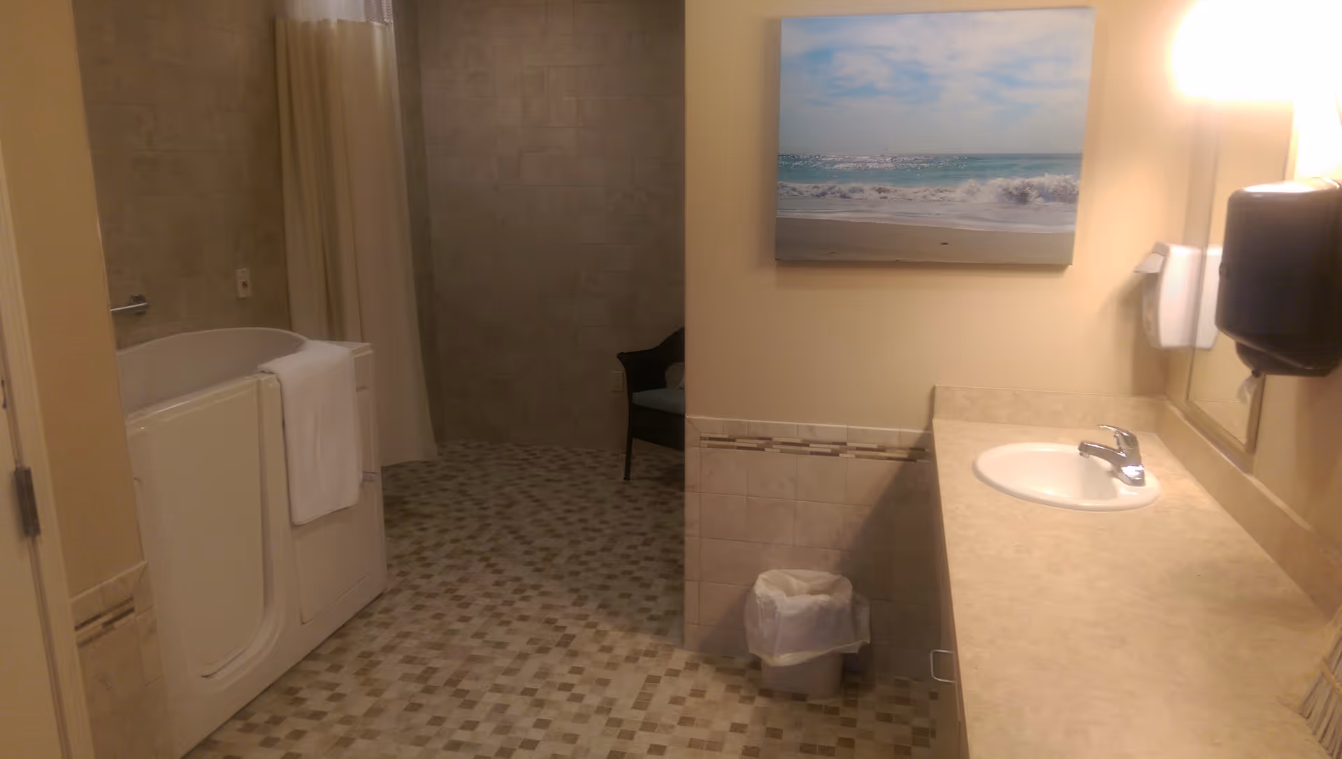 Accessible bathroom with a walk-in tub, tiled floor and shower area, countertop sink, and beach painting on the wall.