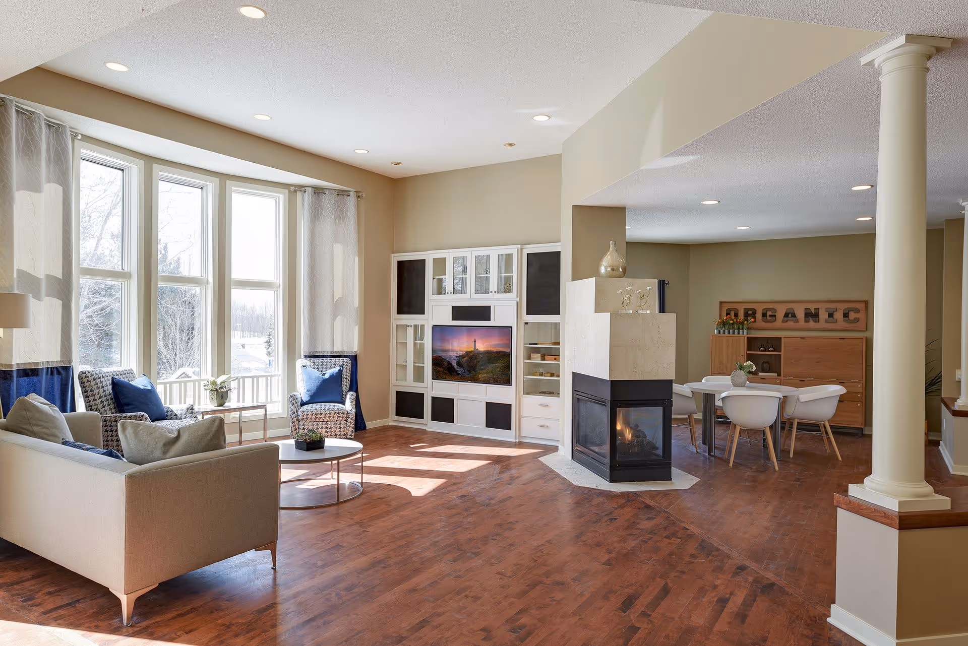 Bright open-plan living room with large bay windows, seating area, fireplace, and adjacent dining area.