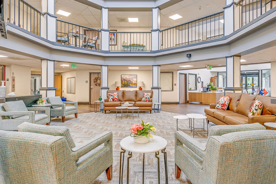 Spacious two-story senior living lobby with sofas, armchairs and small tables arranged around a central seating area.