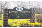 Front view of Bethel Estates Apartments sign with yellow flowers and trimmed hedges.