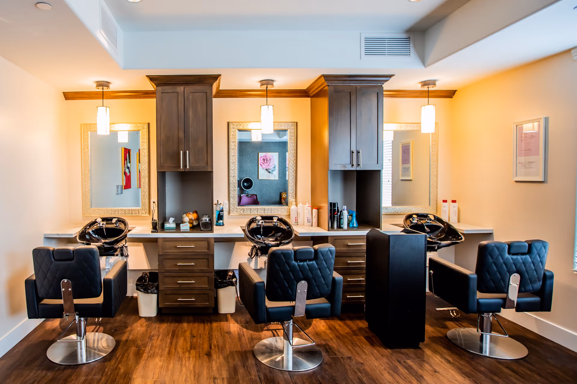 Hair salon station with three styling chairs, shampoo sinks, mirrors, and cabinetry in a bright interior space.