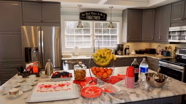 Bright modern kitchen with a marble island laid out with fruit, cake, cups and party supplies.
