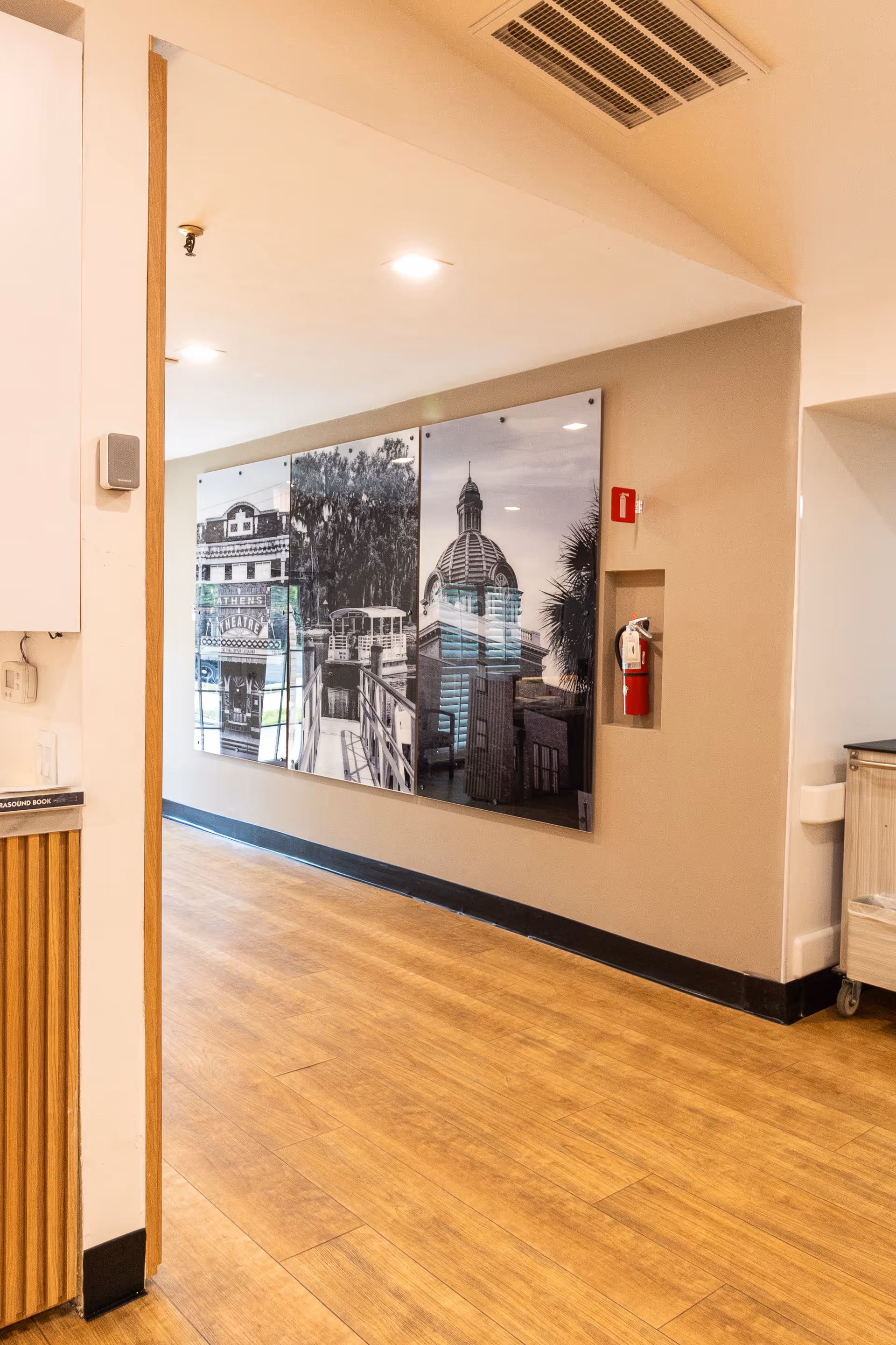 Interior hallway with wood flooring, large black-and-white wall art panels, and a recessed fire extinguisher on the wall.